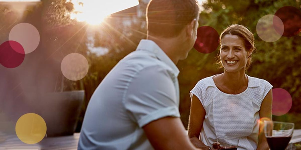 Woman smiling at her partner during an outdoor sunset chat, with warm light and soft pink and yellow circles overlaid.