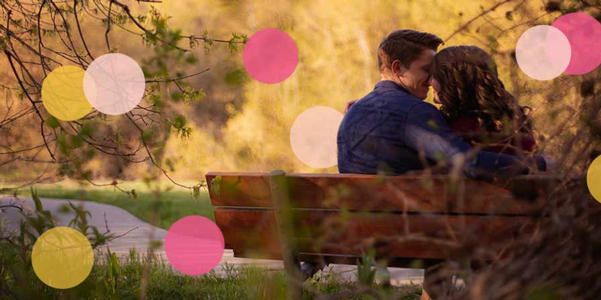 A couple sits close together on a park bench at sunset, sharing an intimate moment surrounded by soft greenery.