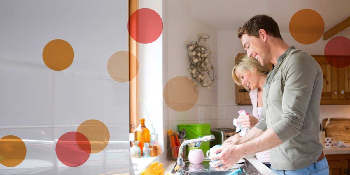Smiling couple washing dishes together in a bright kitchen, sharing a light, happy moment at the sink.