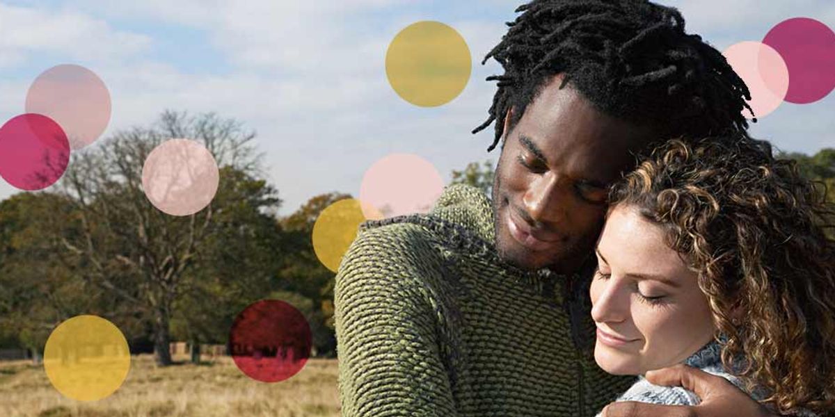 Couple embracing outdoors on a sunny day, eyes closed and smiling softly, with pink and yellow circles overlaid on the image.