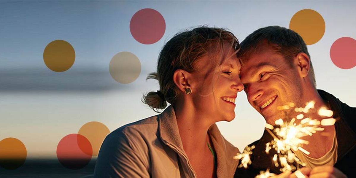 Couple smiling closely while holding sparklers at dusk, sharing a joyful and intimate moment