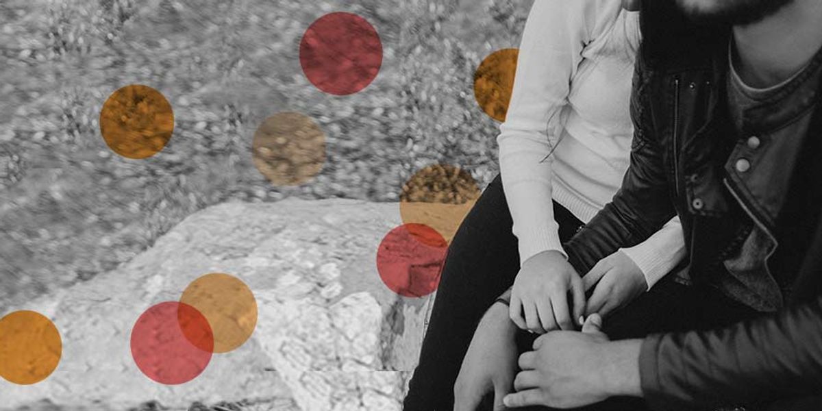 Couple sitting closely on a rock outdoors, holding hands and sharing a quiet, intimate moment