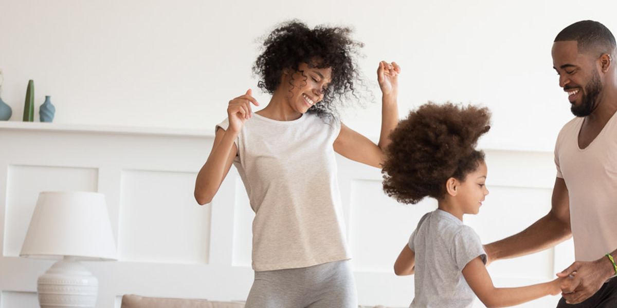 Parents and their young daughter dancing together in a bright living room, smiling and enjoying a playful moment.