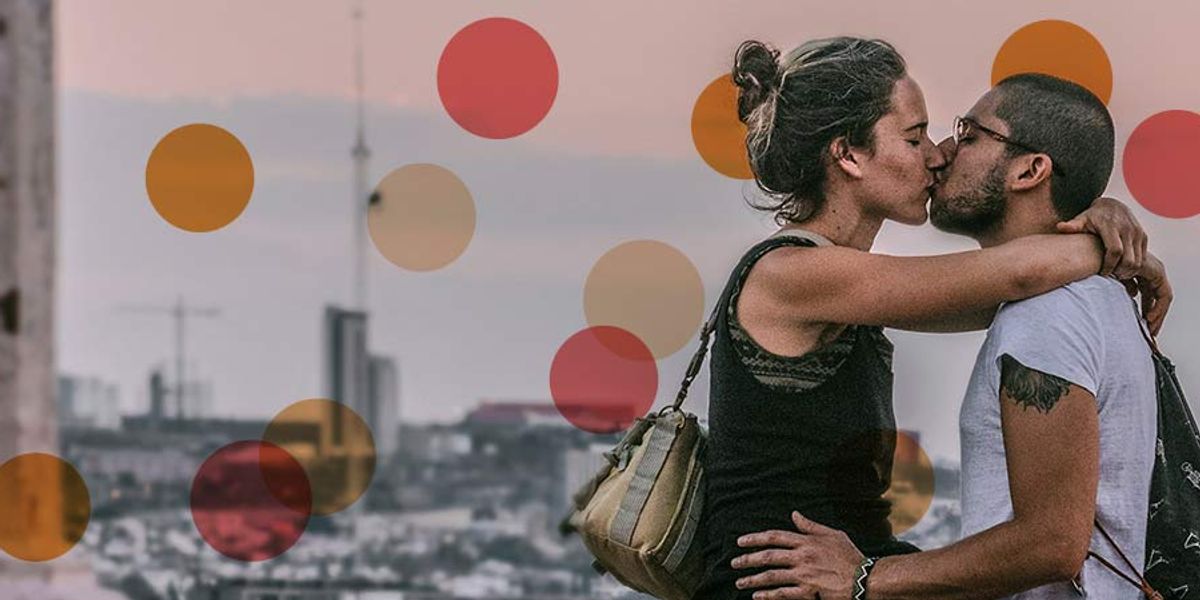 Couple kissing while sitting together overlooking a city skyline at sunset, sharing an intimate moment