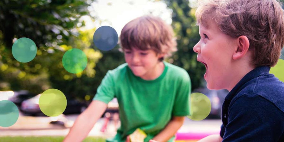 Two young boys play outside on a sunny day, one laughing with excitement as they enjoy their time together.