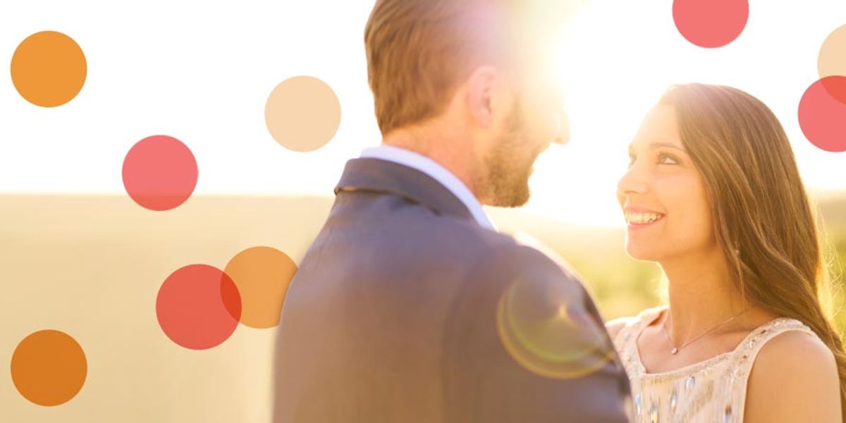 Couple standing together at sunset, smiling warmly as golden sunlight glows behind them.