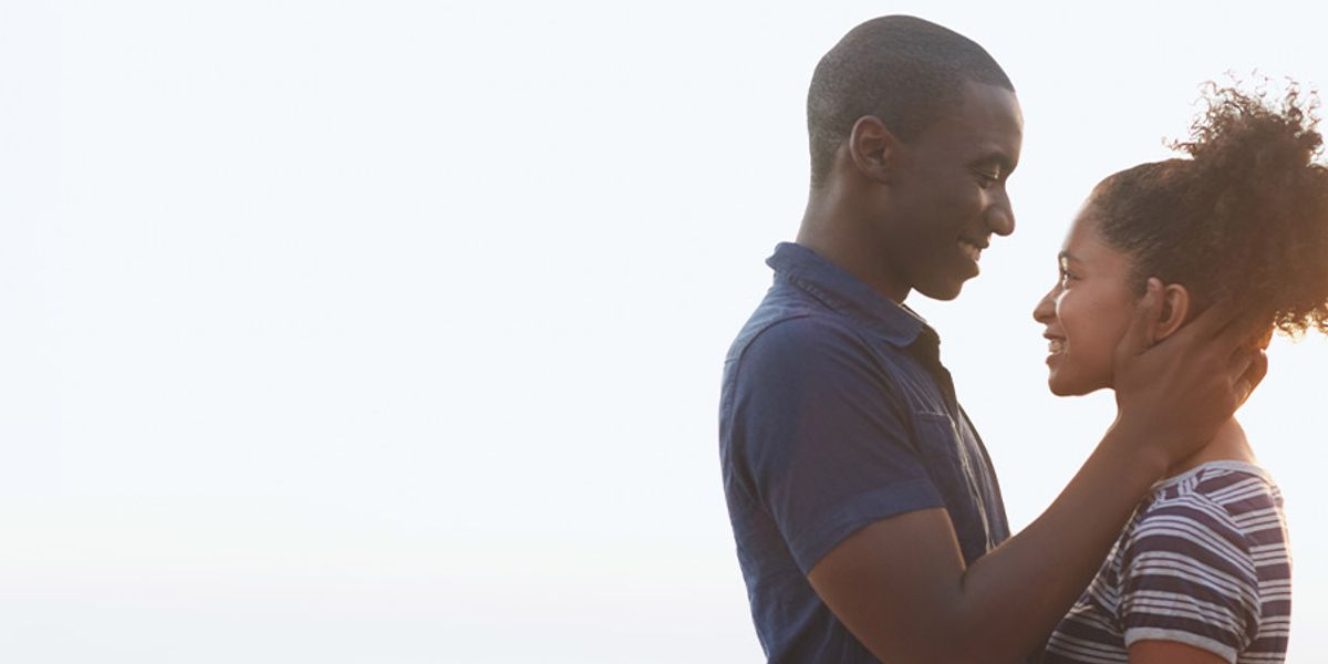 A couple stands close, smiling softly at each other as he gently holds her face.