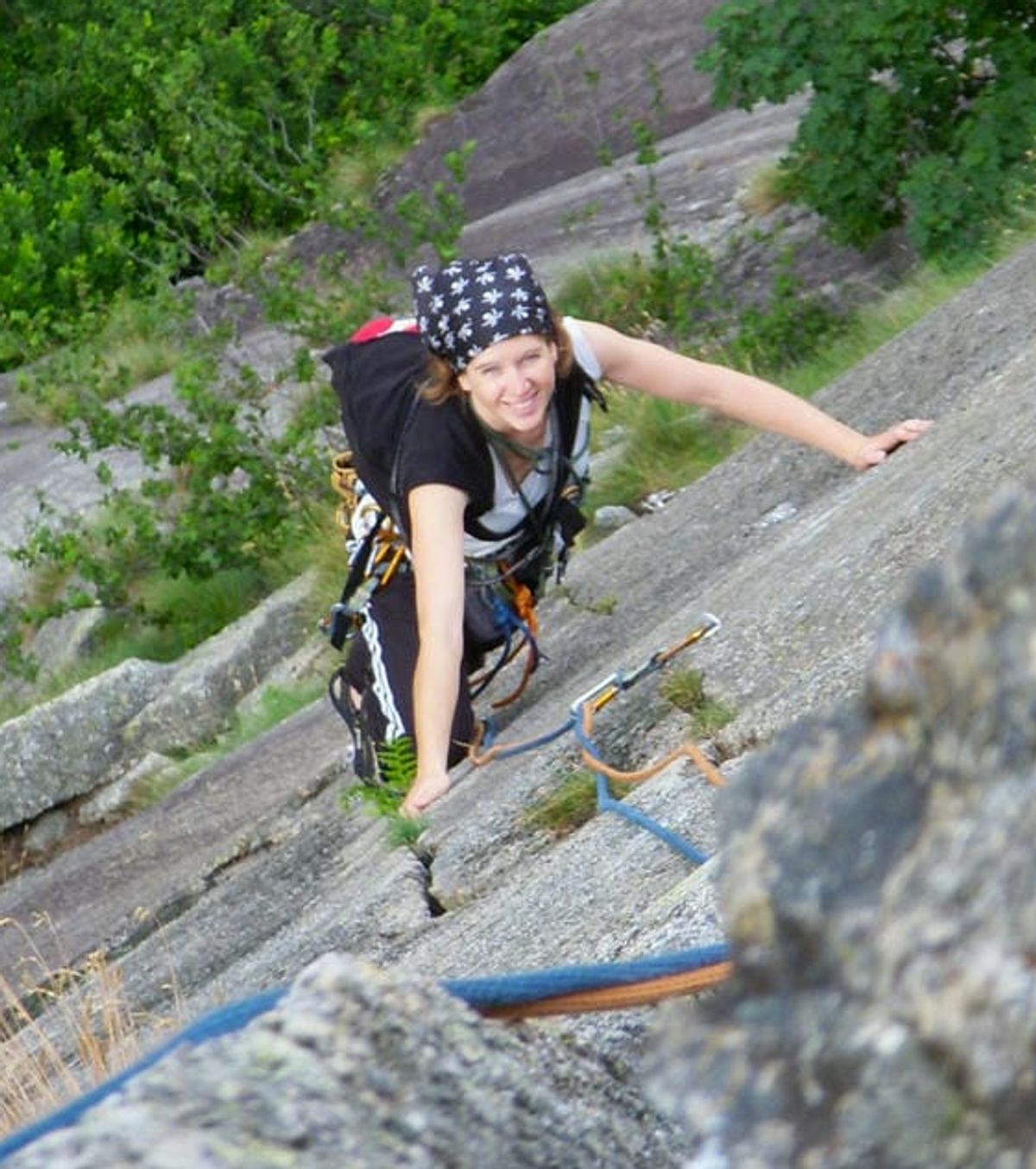 A top down view of Jane Nizi, founder of Figure Eight Creative, climbing up a rock face in the mountains smiling up at the camera.