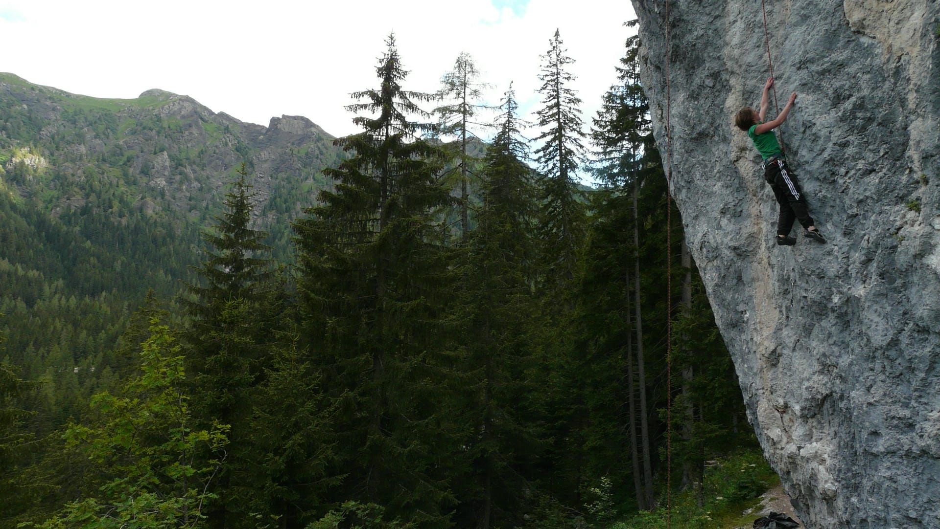 Jane Nizi, founder of Figure Eight Creative, climbing up a rock face in the mountains with trees in the background.