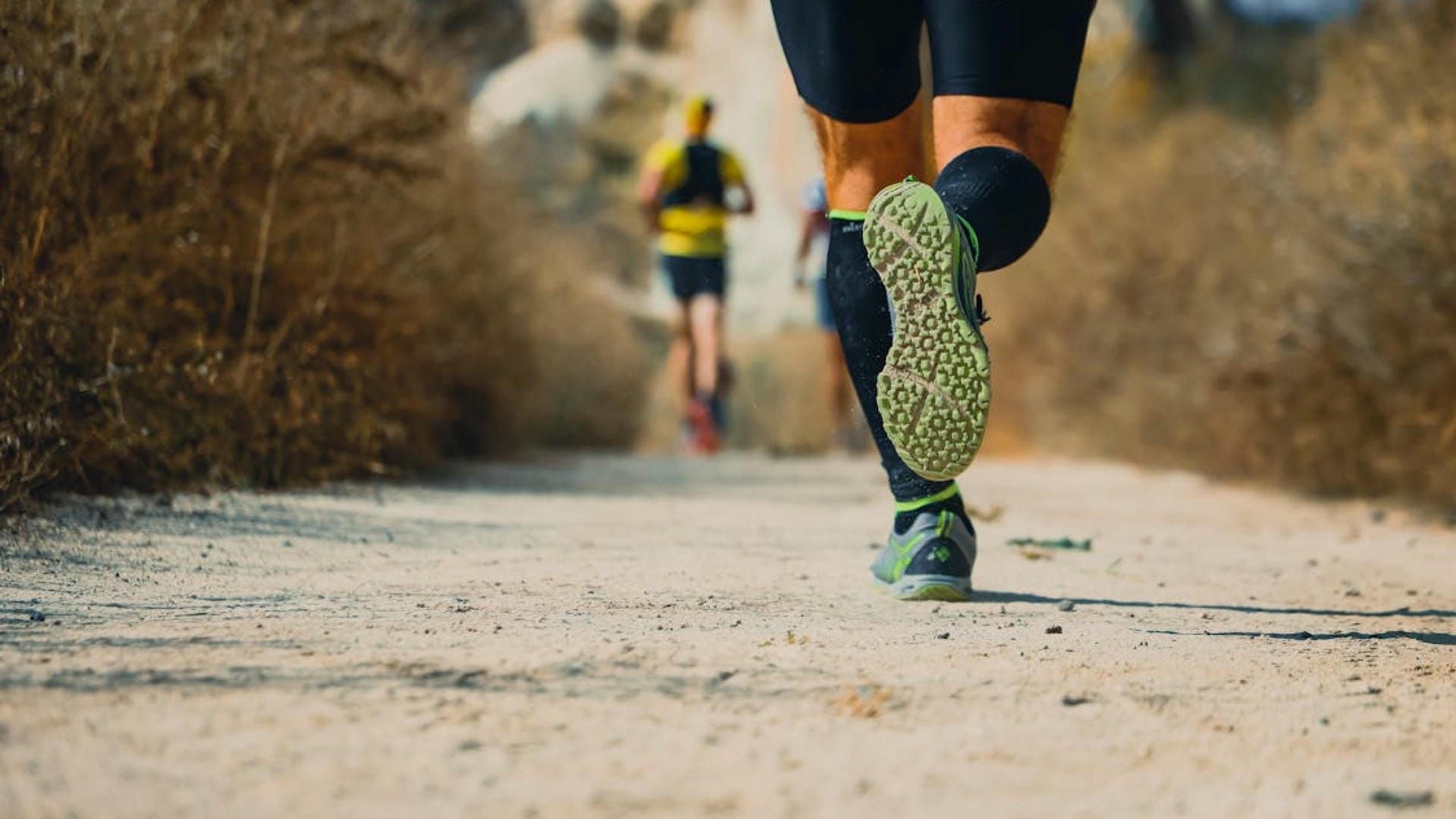 A ground level image of an outdoor trail runner running down a dirt trail.