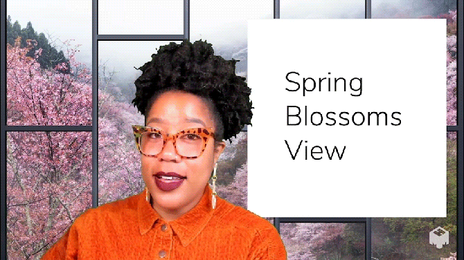 Person with orange shirt and glasses sniffing bouquet in front of window with cherry blossom trees 