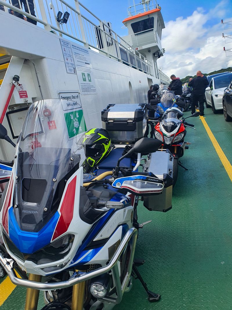 Touring motorcycles parked in a row on the deck of a small car ferry on a sunny day
