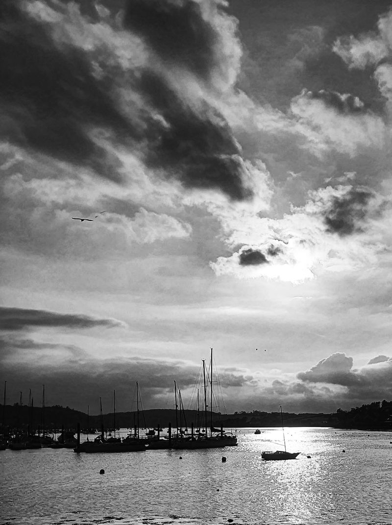 Black and white view of sailing boats moored in an Irish harbour at dusk under dramatic clouds