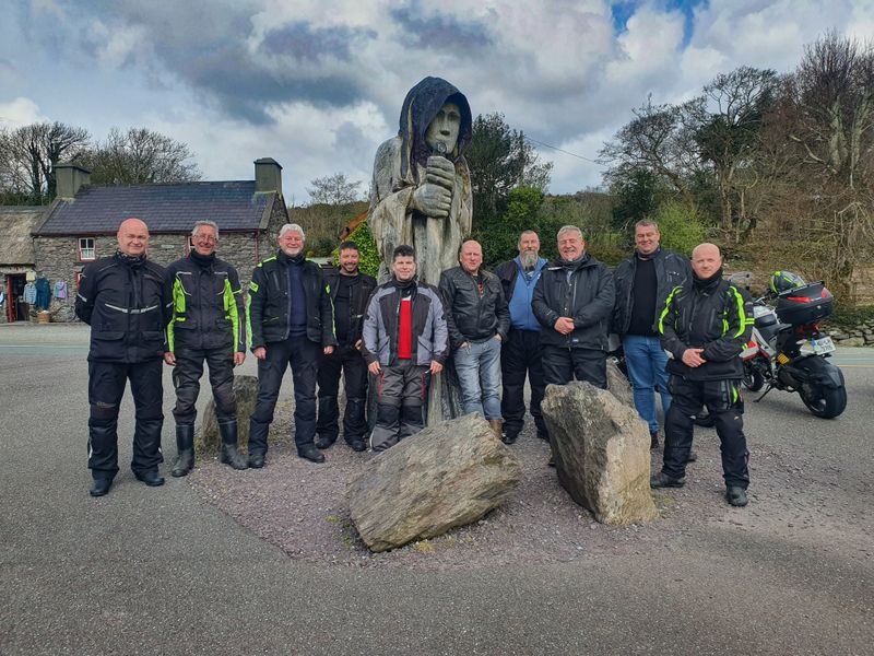 Wild Atlantic Biker tour group posing beside a carved wooden statue outside a stone cottage in Ireland