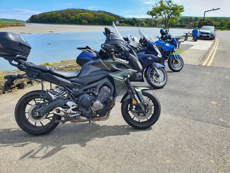 Riders' own touring motorcycles parked beside a calm tidal estuary on a sunny day in the south of Ireland