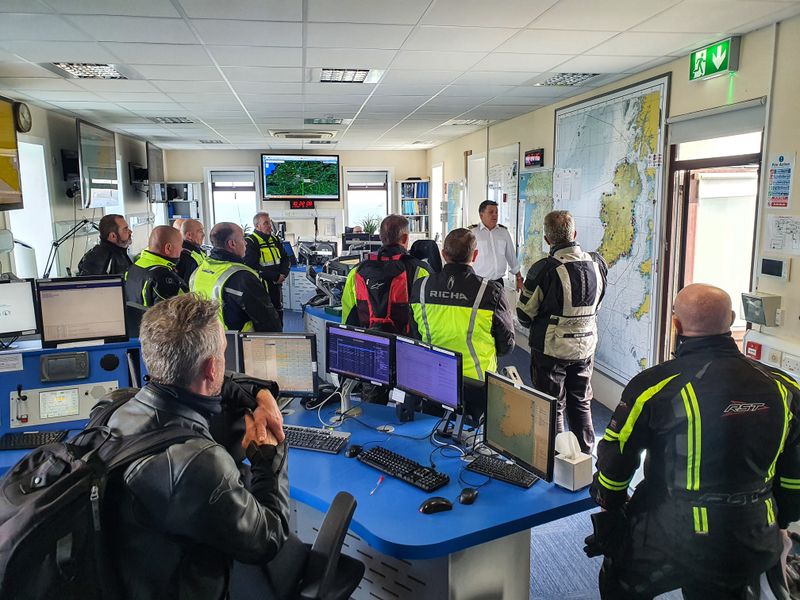 Motorcycle tour group visiting a coast guard operations room lined with monitors and sea charts of Ireland
