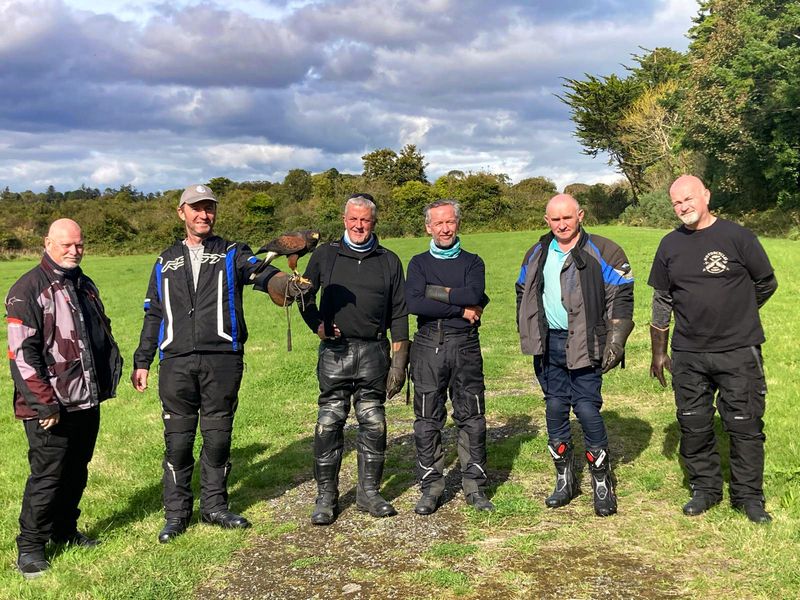 Tour group of motorcyclists in a field, one rider holding a Harris hawk during a falconry experience