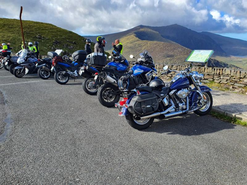 Touring motorcycles parked at a stone-walled mountain pass viewpoint with riders chatting