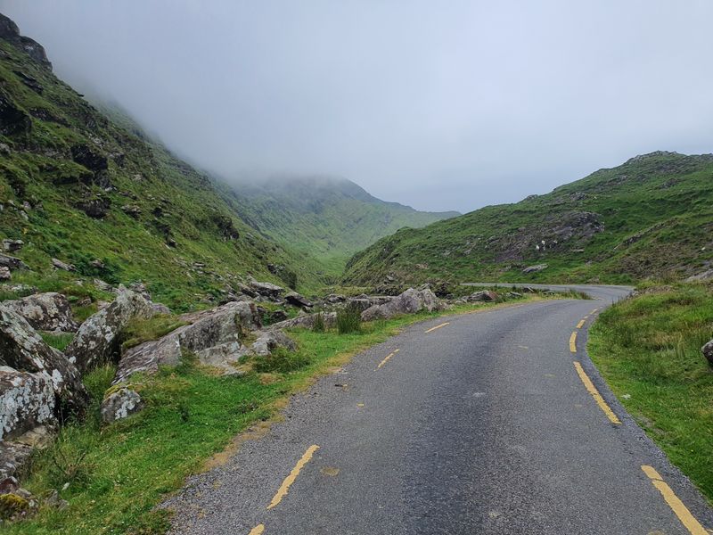 Empty single-track road curving through a misty rocky mountain pass in County Kerry