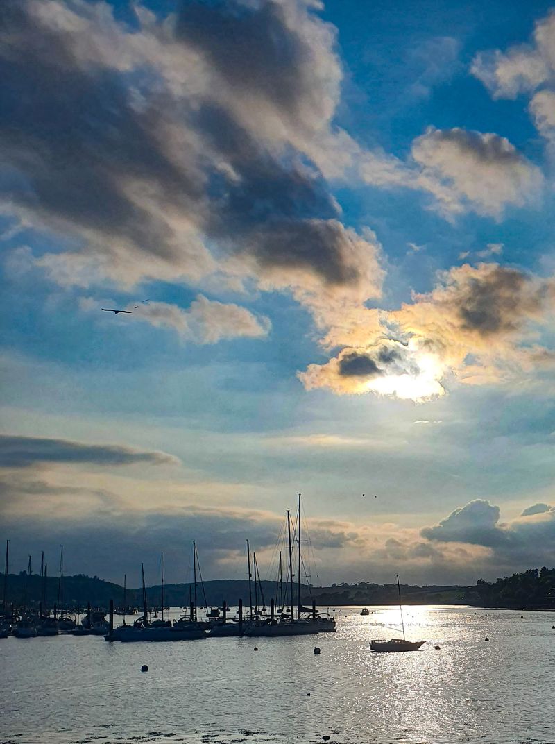 Evening sun breaking through clouds over sailboats moored in an Irish harbour