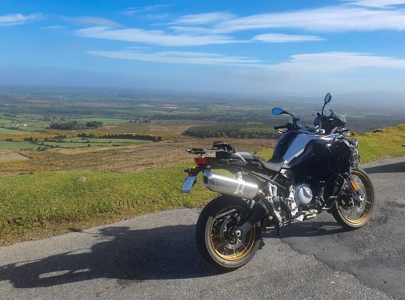 Adventure motorcycle parked at a mountain viewpoint above a patchwork of Irish farmland