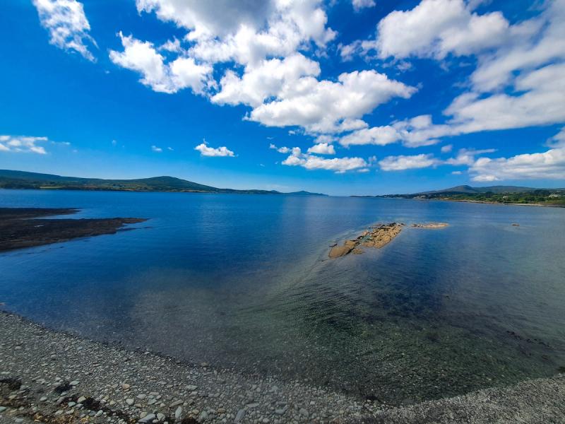 Calm blue bay with rocky shoreline and green hills on the south-west Irish coast under a bright summer sky