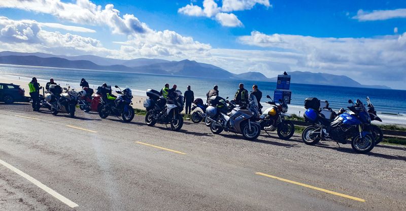 Motorcycles lined along the coast road above Inch Beach with mountains across Dingle Bay