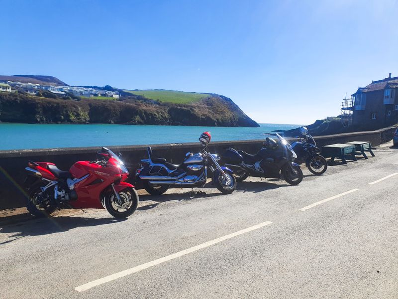 Riders' motorcycles lined along a seawall above a turquoise cove on the Wild Atlantic Way
