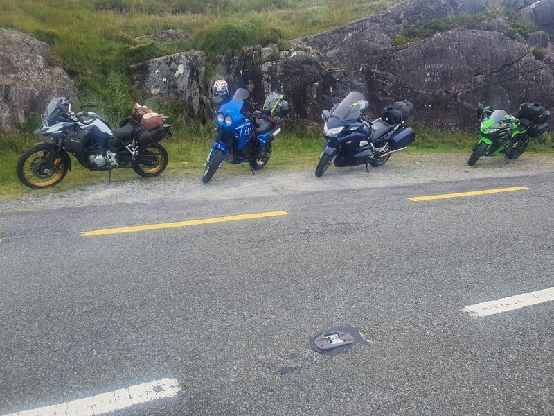 Four touring motorcycles parked beneath a rock painted with a wild sheep warning on a remote Irish road