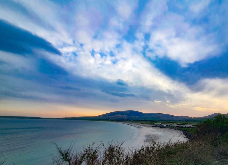 Curved sandy beach and calm bay at dusk beneath a dark mountain in Kerry