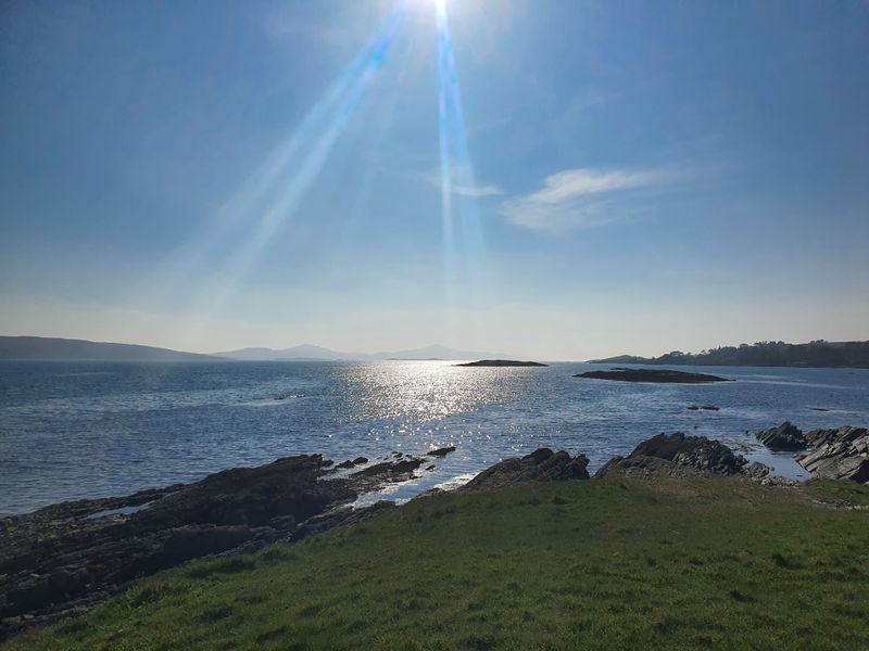 Sunbeams breaking over a sparkling sea and rocky headland on the West Cork coast