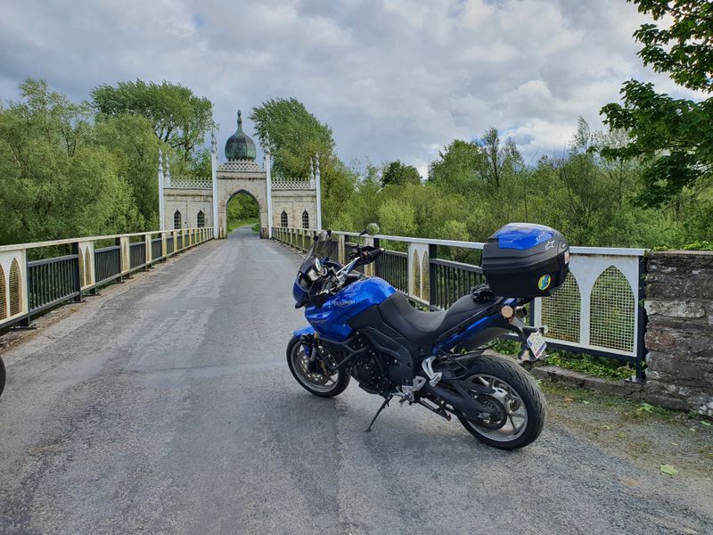 Blue Triumph Tiger motorcycle parked on a bridge in front of the Hindu-Gothic Dromana Gate