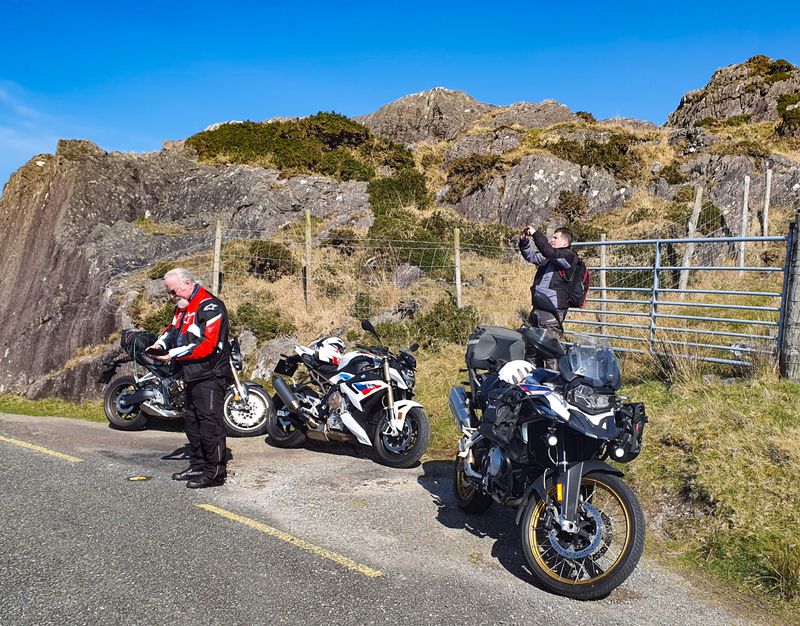 Riders and their BMW motorcycles stopped at the rocky summit of the Healy Pass under a blue sky