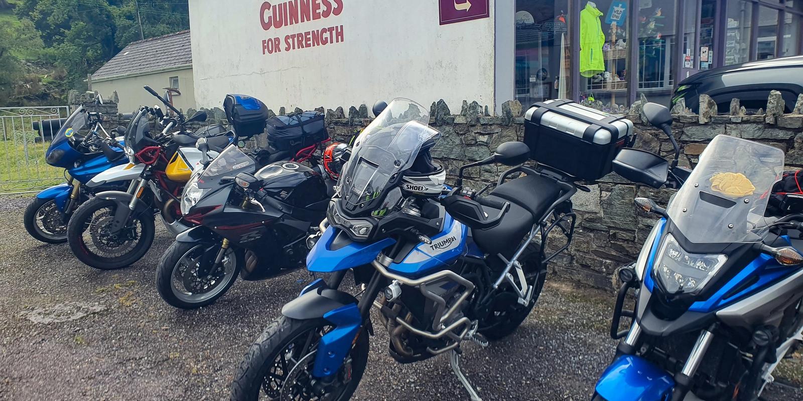 Touring motorcycles parked at a coffee stop outside a rural shop with a vintage Guinness mural