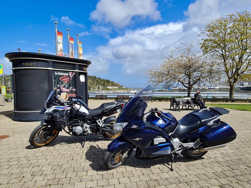 Two touring motorcycles parked by a Cork harbour marina on a sunny day
