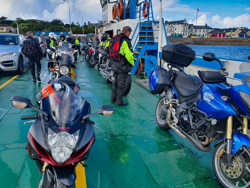 Motorcycles and riders in high-visibility gear lined up on the deck of a small Irish car ferry