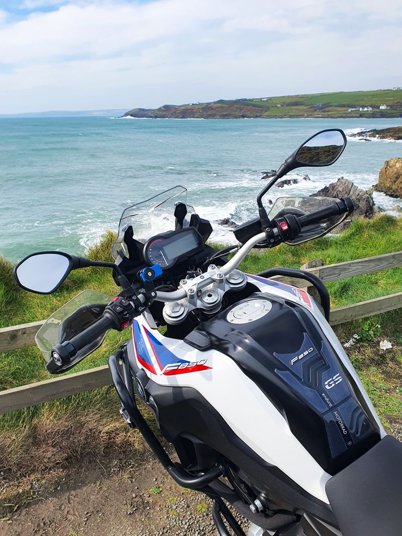 View over the handlebars of a BMW F850GS looking out on a turquoise Irish coastal bay