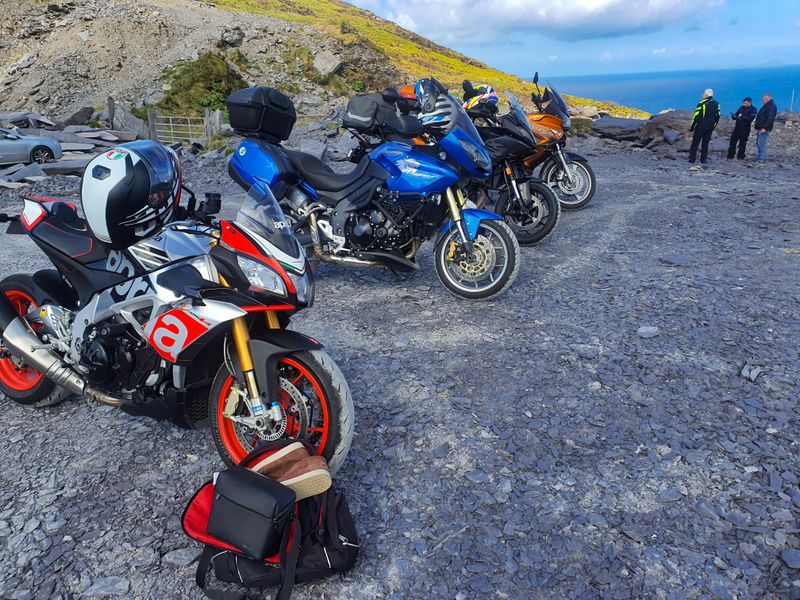 Motorcycles parked on slate ground at a quarry viewpoint high above the Atlantic, riders admiring the sea view