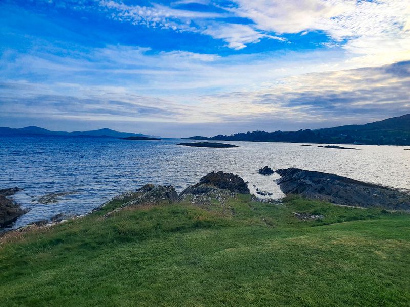 Green headland and rocky shoreline meeting a calm island-dotted bay in West Cork