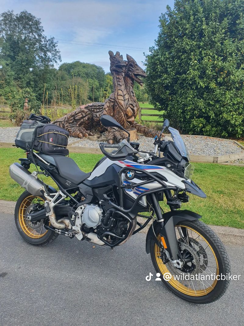 George's BMW F850GS Adventure parked beside a carved wooden dragon sculpture on an Irish country road