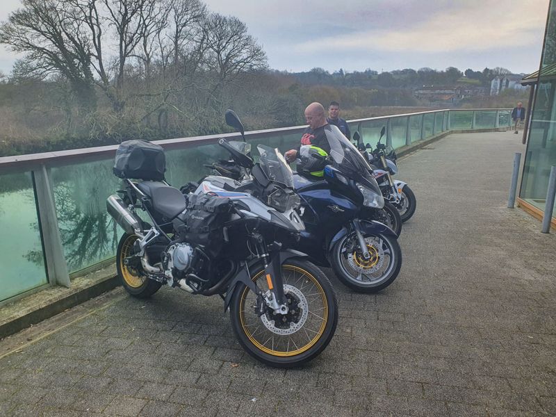 Group of touring motorcycles parked on a riverside boardwalk during a ride stop