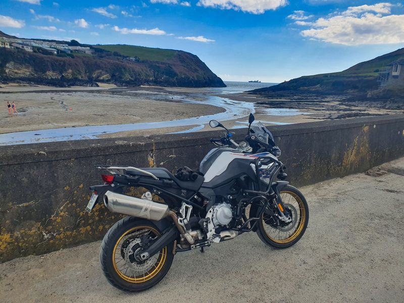 BMW F850GS parked on a seawall above a tidal sandy cove on the Irish coast