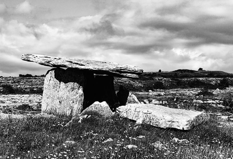 Black and white photo of Poulnabrone Dolmen ancient portal tomb under dramatic clouds in the Burren