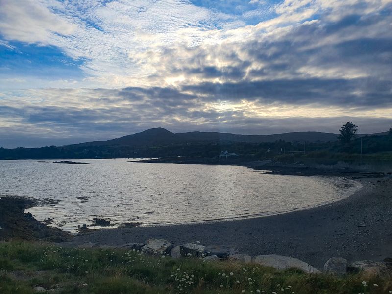 Calm pebble beach cove at dusk with moody clouds over dark hills on the West Cork coast