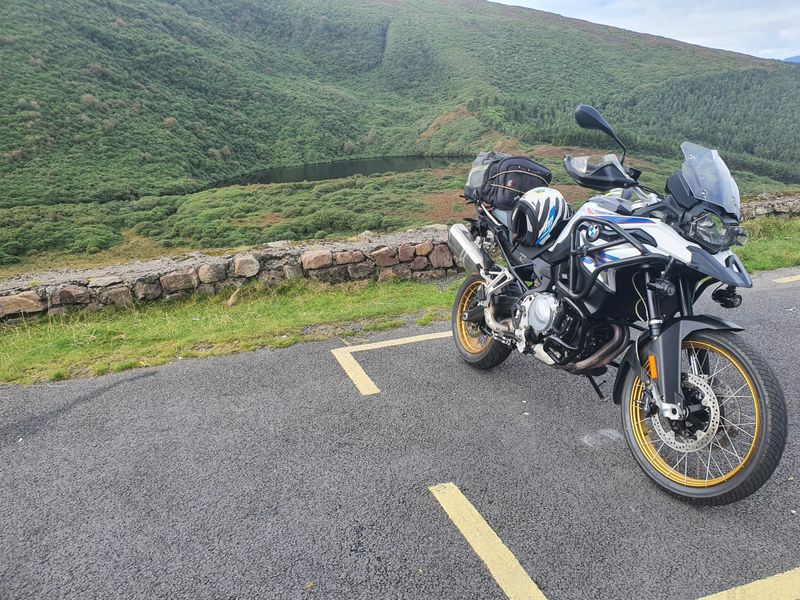 Adventure motorcycle parked on a mountain pass road above a dark corrie lake in southwest Ireland