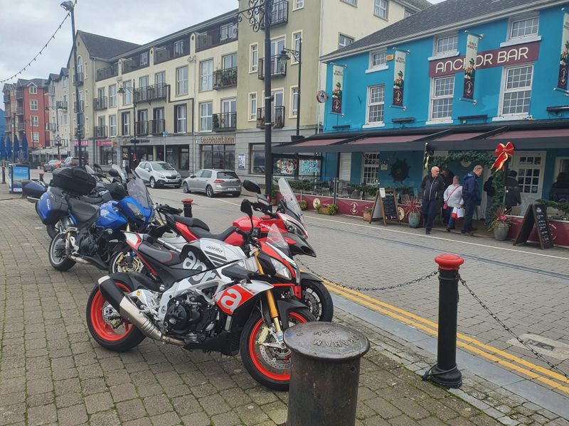 Touring motorcycles parked along a quayside outside the Anchor Bar in an Irish harbour town
