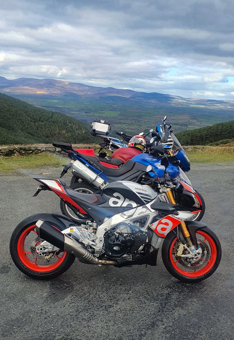 Sport and adventure motorcycles parked at a scenic mountain overlook above green Irish farmland