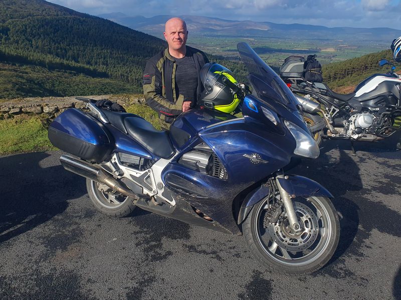 Rider with a Honda ST1300 tourer at a mountain pass viewpoint over a green Irish valley