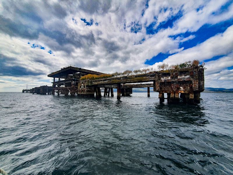 Abandoned overgrown concrete pier ruins rising from the sea under a dramatic cloudy sky