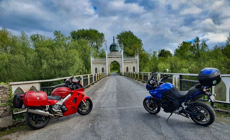 Red and blue touring motorcycles parked on a bridge in front of the ornate Dromana Gate with its copper onion dome
